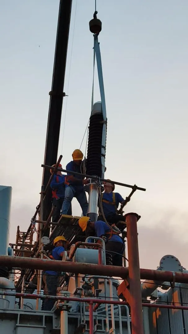 A crew replacing a high-voltage bushing on a transformer using a lifting rig.