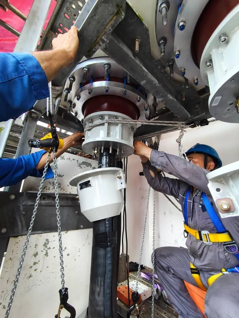 Technicians working beneath an extra-high-voltage bushing flange.